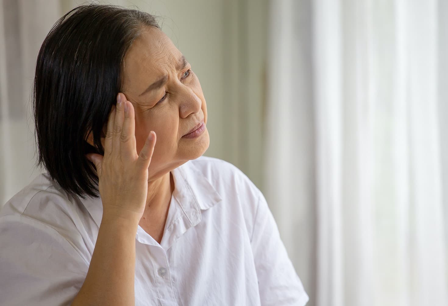older woman gazes out window, looks confused