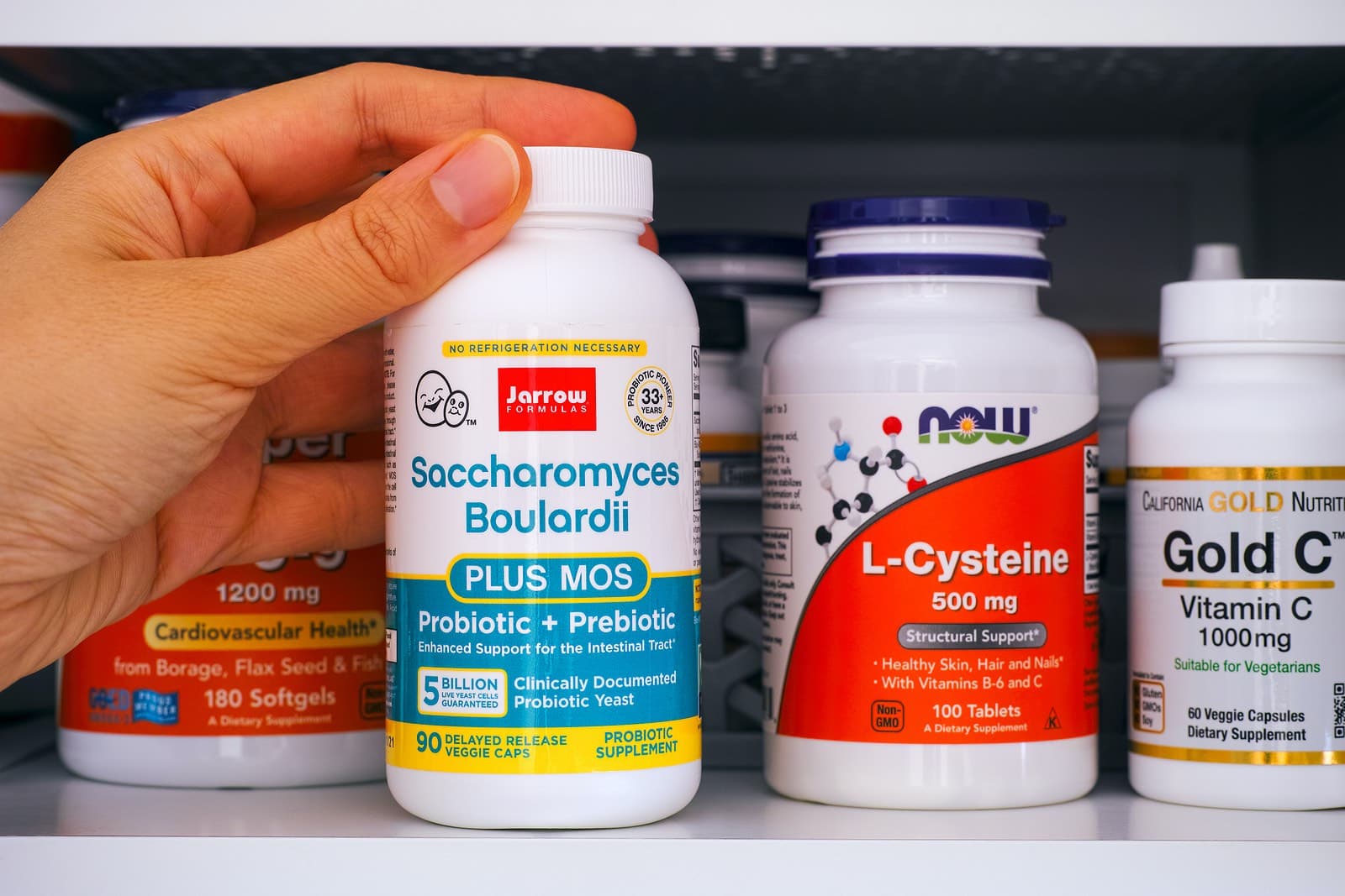 Several bottles of supplements with hand touching Saccharomyces boulardii