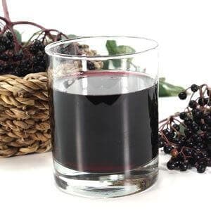 a glass of elderberry juice and elderberries