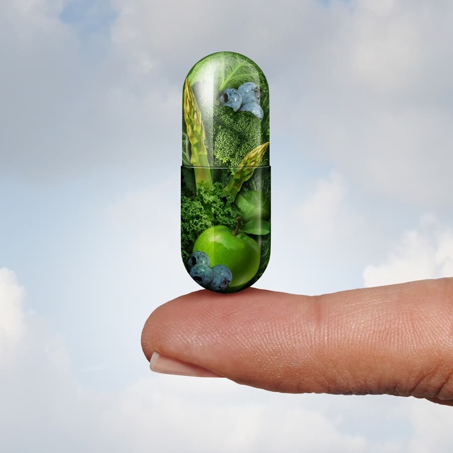 green capsule containing vegetables and fruits balanced on fingertip