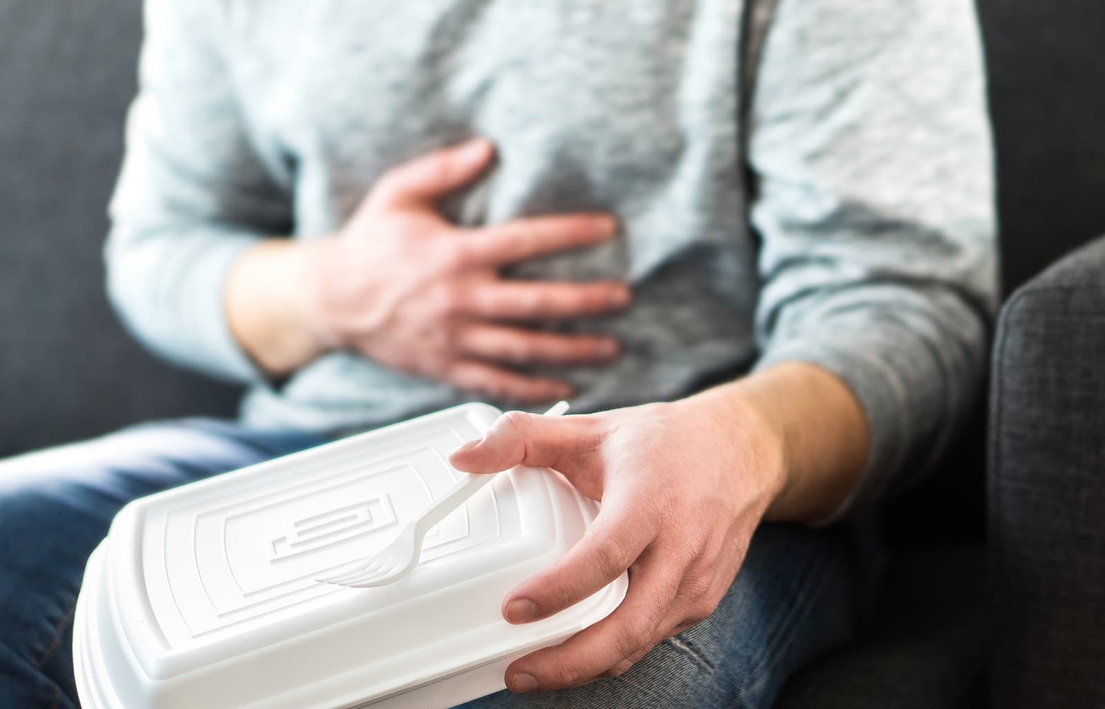 man holding fast food container and clutching his chest because of heartburn