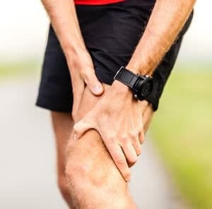 Runner holding sore leg knee pain from running or exercising jogging injury or cramp