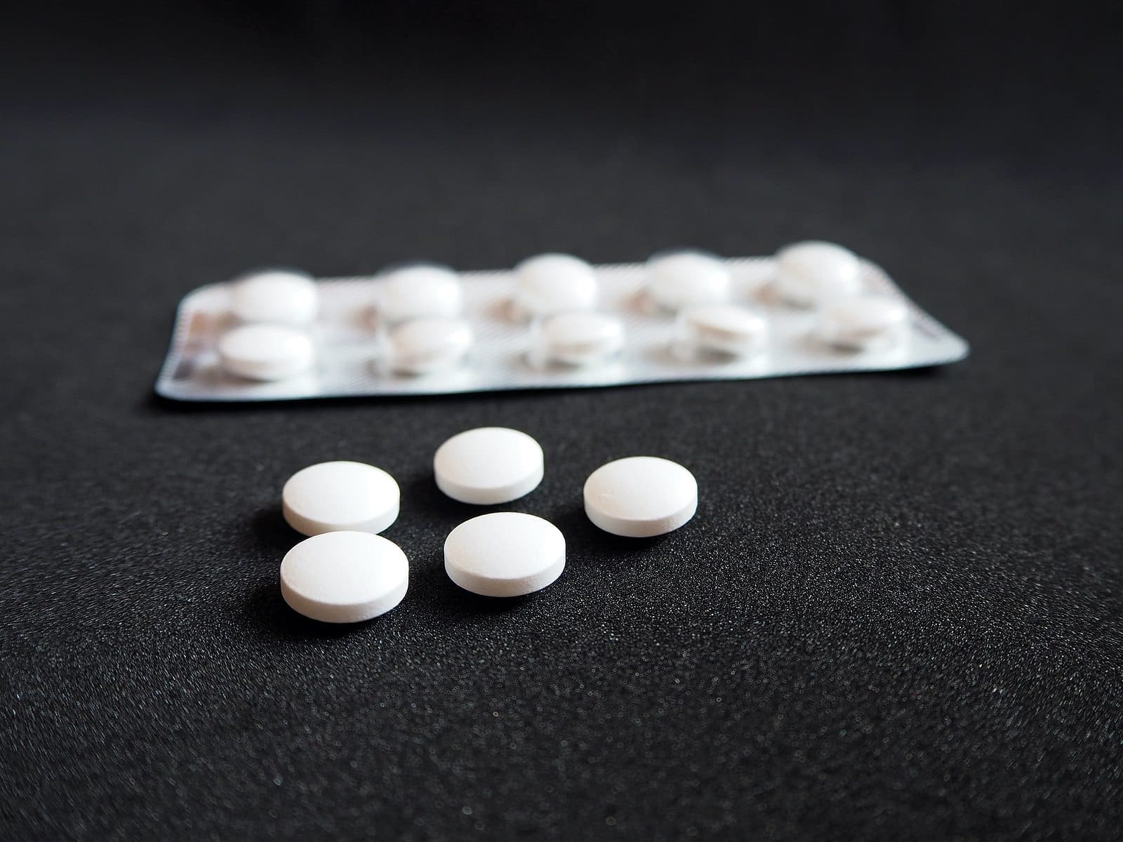 White blister pack with medicine pills on a black background, modern medicine used to prevent and treat diseases. Packaging for drugs: painkillers, antibiotics, vitamins and aspirin tablets. Opioid epidemic and drug abuse concept.
