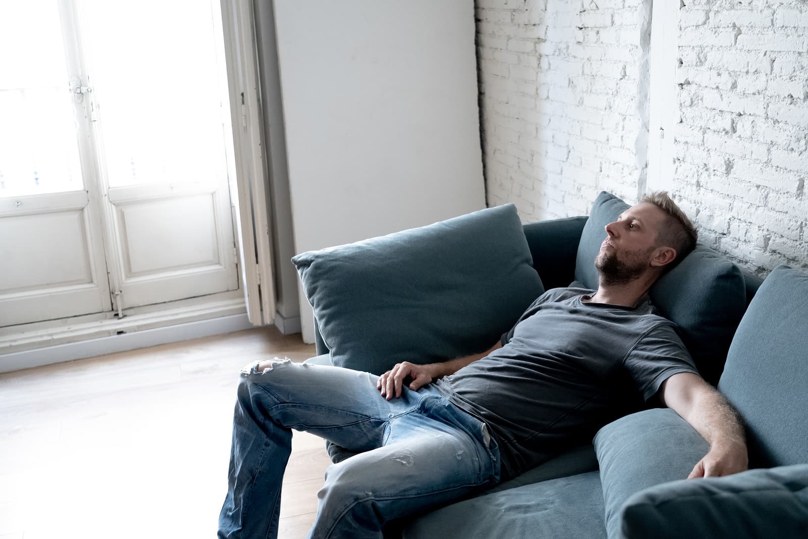 young man suffering from depression sitting on a couch looking sad, finds it hard to deal with depression