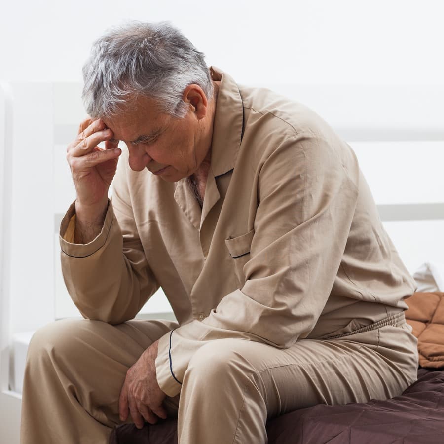 Senior man in pajamas sits on bed unable to sleep