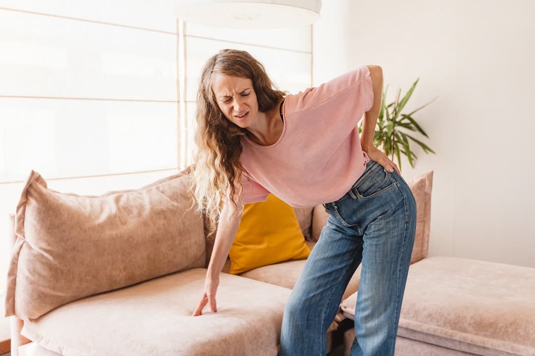 Chronic back pain. Adult woman is holding her lower back, while standing and suffering from unbearable pain. Back ache
