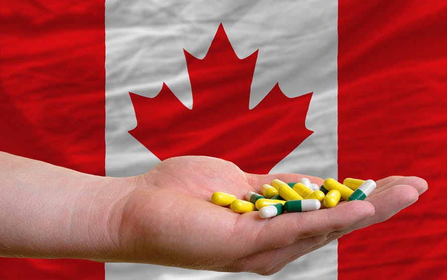 Man holding capsules in front of complete wavy national flag of canada symbolizing health medicine cure vitamines and healthy life

