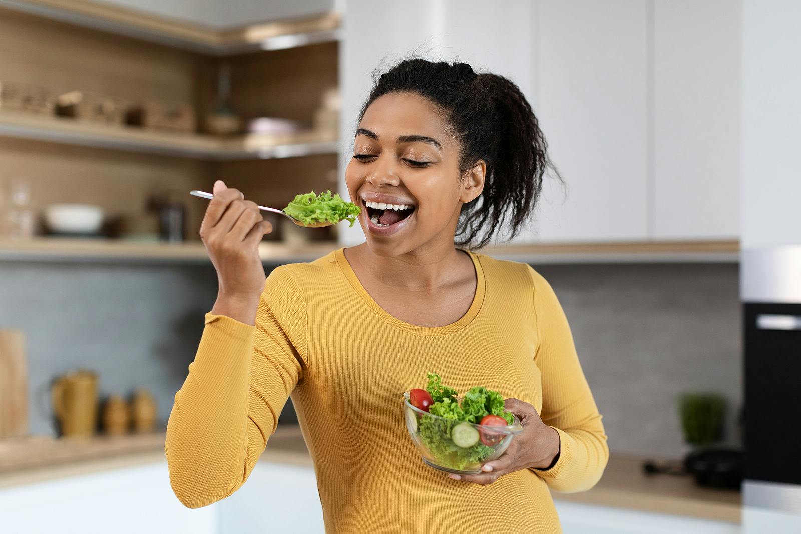 Portrait of cheerful young black pregnant woman with big belly eating salad with organic vegetables
