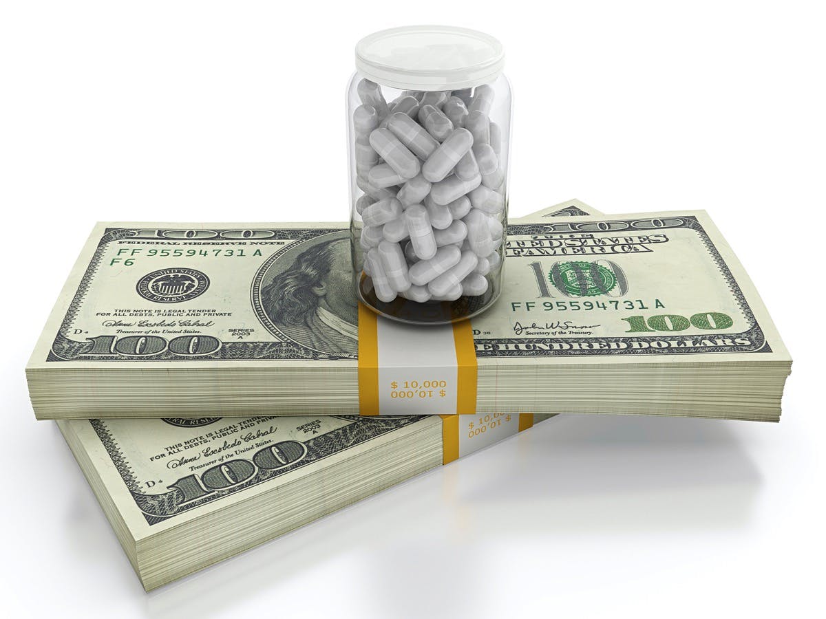 White pills on top of dollar bills bundle. High cost of healthcare concept
