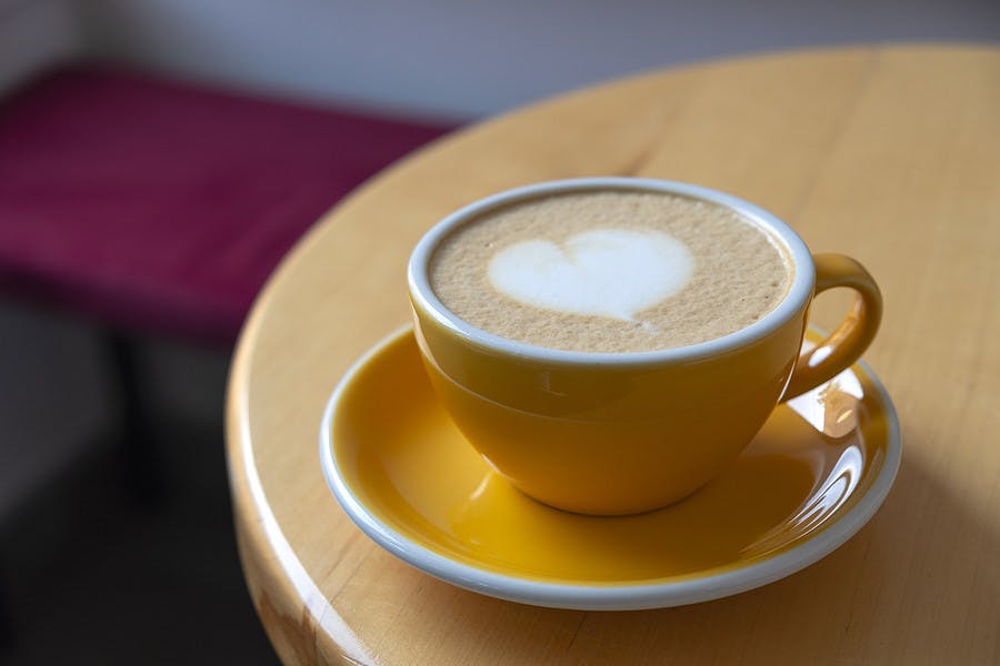 Freshly served cup of cappuccino with latte art on a wooden table in a cafe. A beautiful yellow cup of cappuccino.
