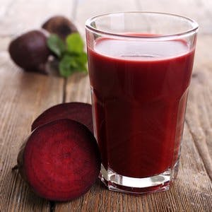 Glass of beet juice with beets on wooden table close up
