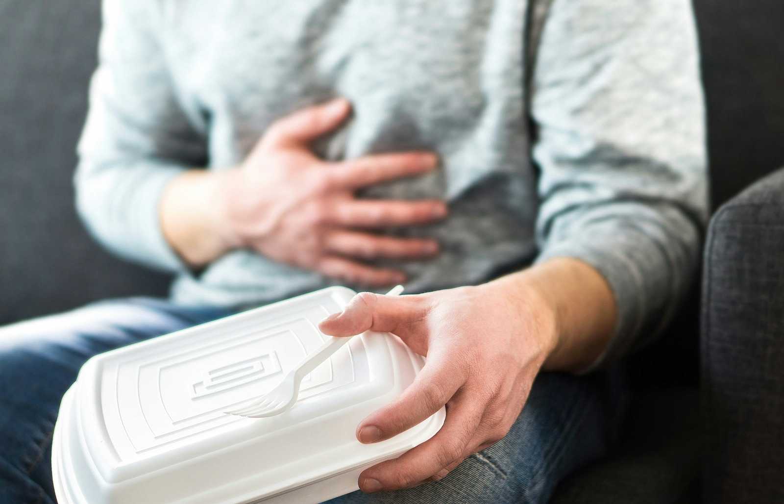 Man holding fast food container and clutching his chest because of heartburn