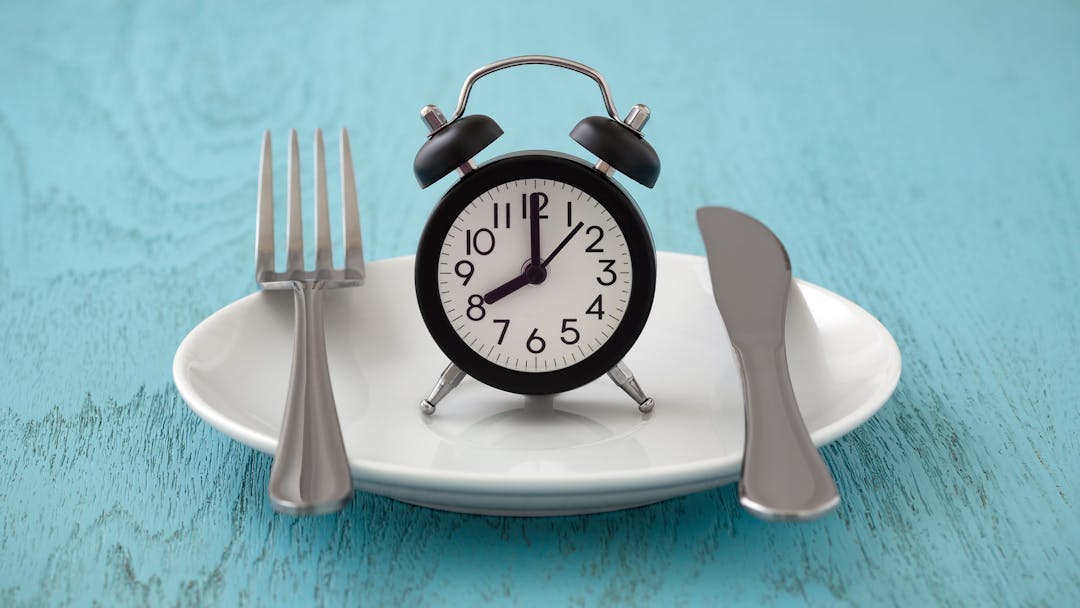 Clock on notepad with fork and knife, intermittent fasting and weight loss plan concept
