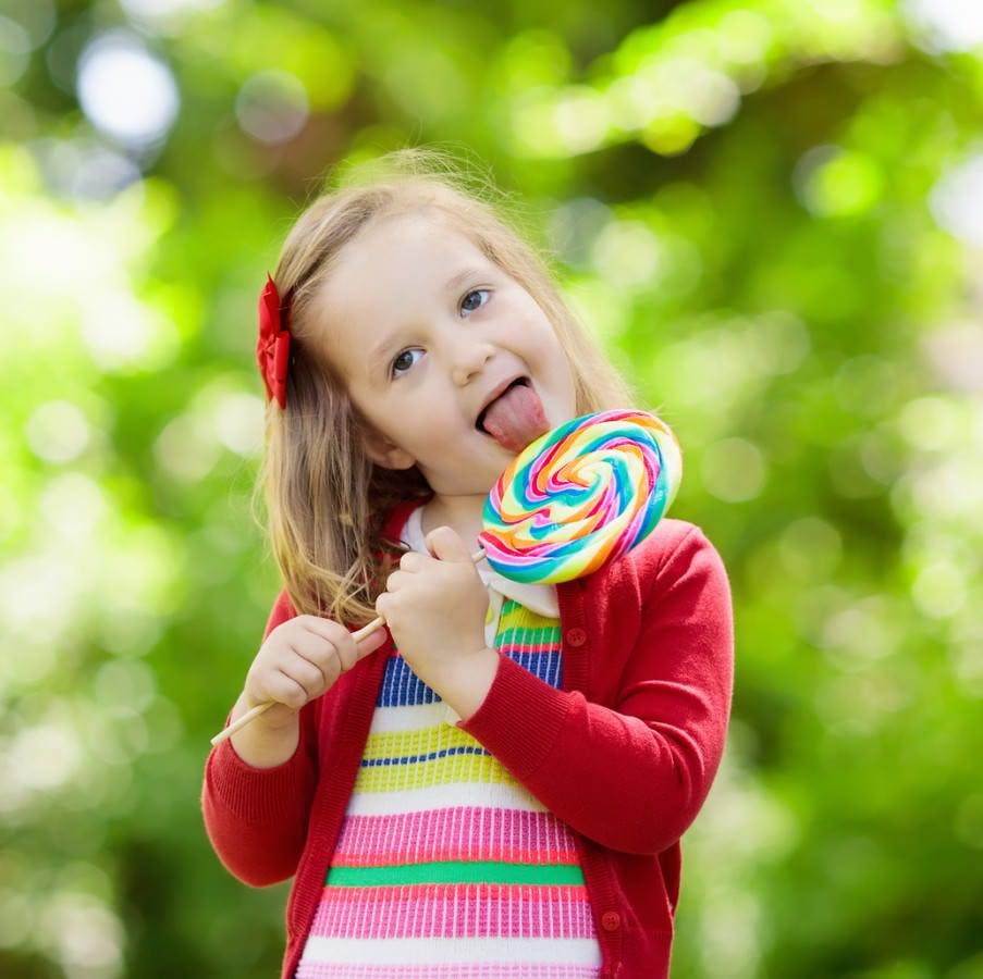 Cute little girl with big colorful lollipop. Child eating sweet candy bar. Sweets for young kids. Summer outdoor fun. Preschooler kid with sugar lolly. Children having snack in a park after preschool.
