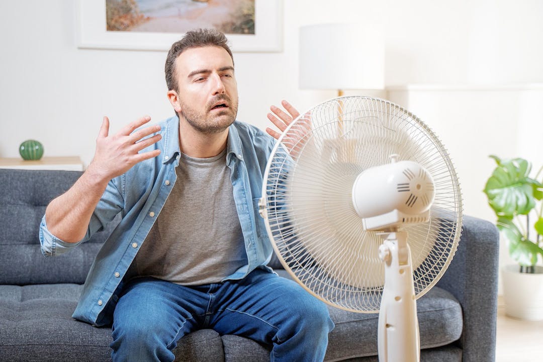 One man suffering summer heat at home trying to cool off drinking water
