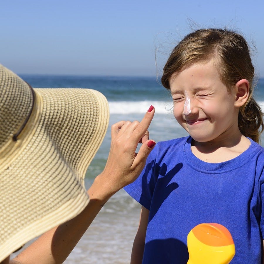 Mother applying sunscreen on child on the beach
