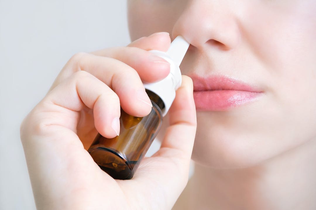 Nasal spray.  Beautiful young woman. Closeup. Face with nasal drops. Close-up of female spraying medical nasal spray in her nose. Cold and flu, health care concept.
