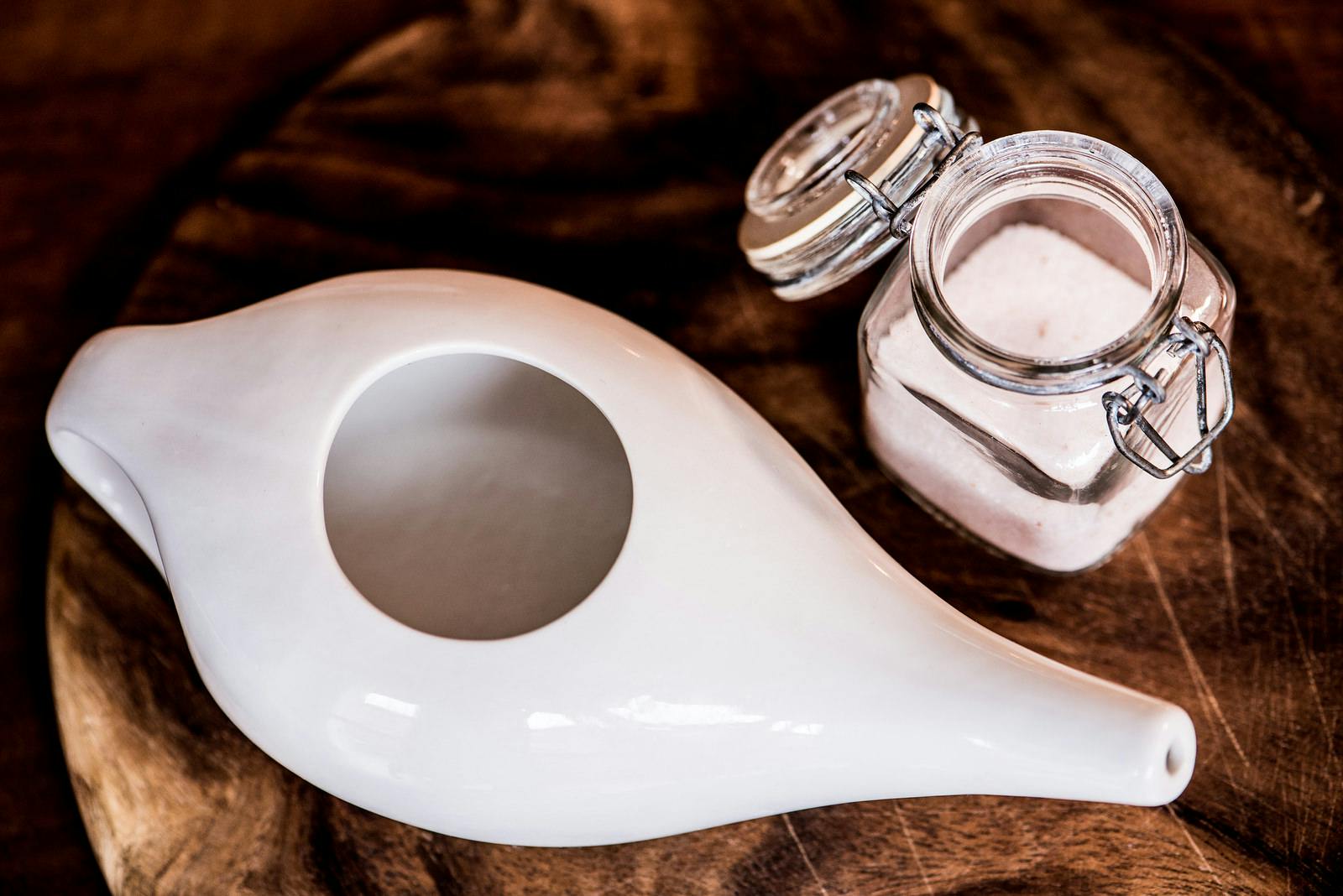 Neti pot, ayurvedic tools for cleaning nose with water and salt, view from top, wooden table and board on background
