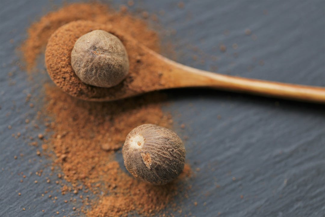 Nutmeg .Whole and ground nutmeg in a wooden spoon on a schiffer background. and herbs concept.Food ingredient. for meat and baking.Nutmeg powder

