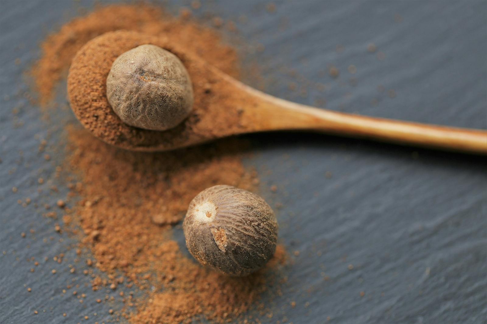 Nutmeg .Whole and ground nutmeg in a wooden spoon on a schiffer background. and herbs concept.Food ingredient. for meat and baking.Nutmeg powder
