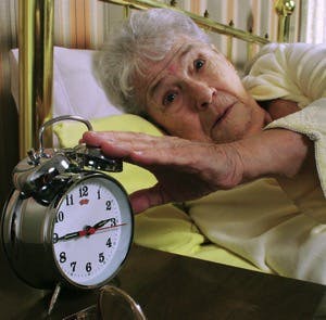 Surprised senior woman trying to close her alarm clock
