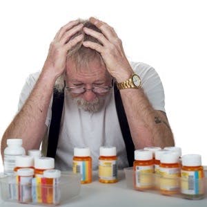 Senior sitting behind a lot of pill bottles holding his head in his hands isolated on white
