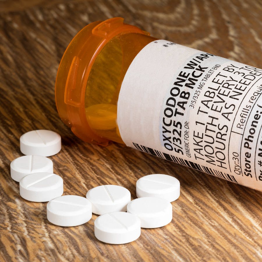 Close photo of prescription bottle for Oxycodone tablets and pills on wooden table for opioid epidemic illustration
