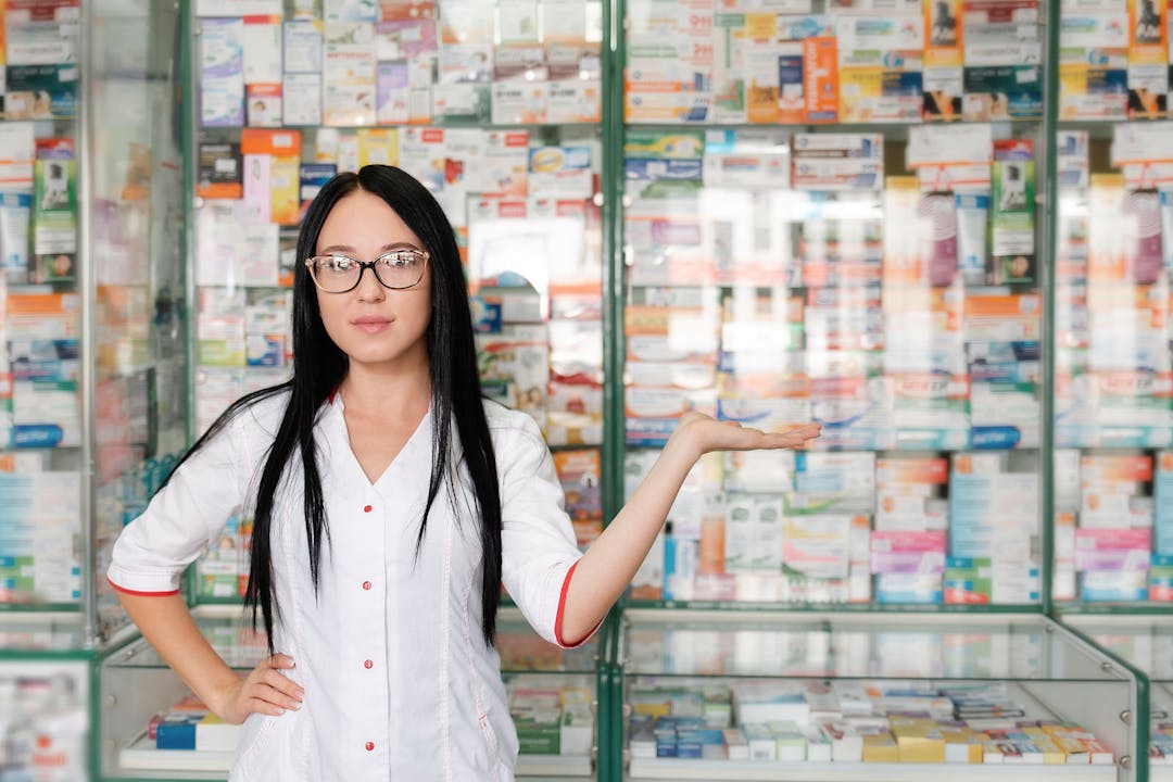 Pharmacy and pharmacist-seller. Female pharmacist with glasses posing on the background of shop Windows and pointing. Copy space
