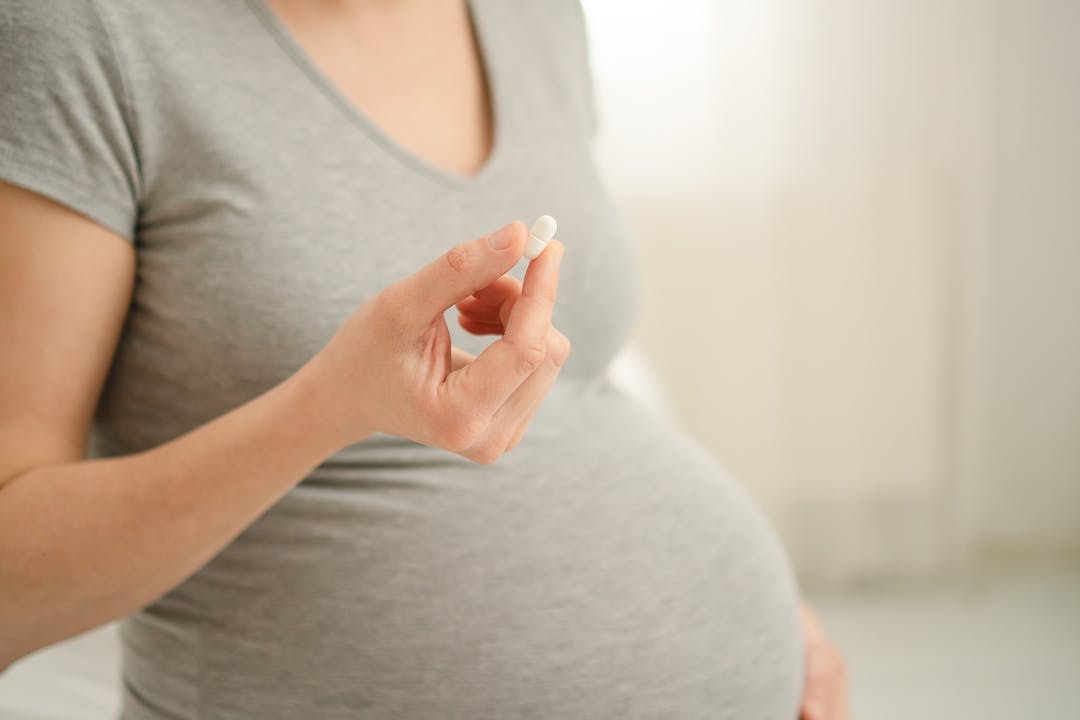 Close-up view of pill in hand. In the background is a pregnant woman. Taking vitamins during pregnancy. Health care and medication during pregnancy and childbearing.
