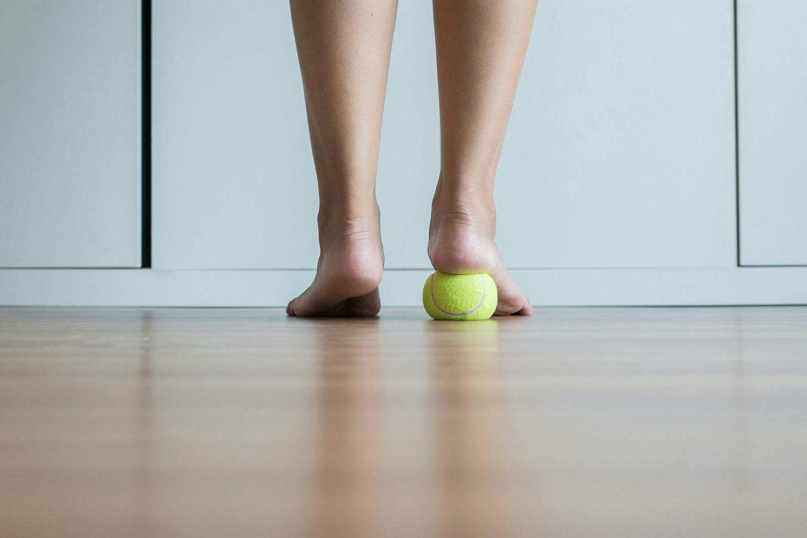 woman standing on tennis ball to relieve plantar fasciitis