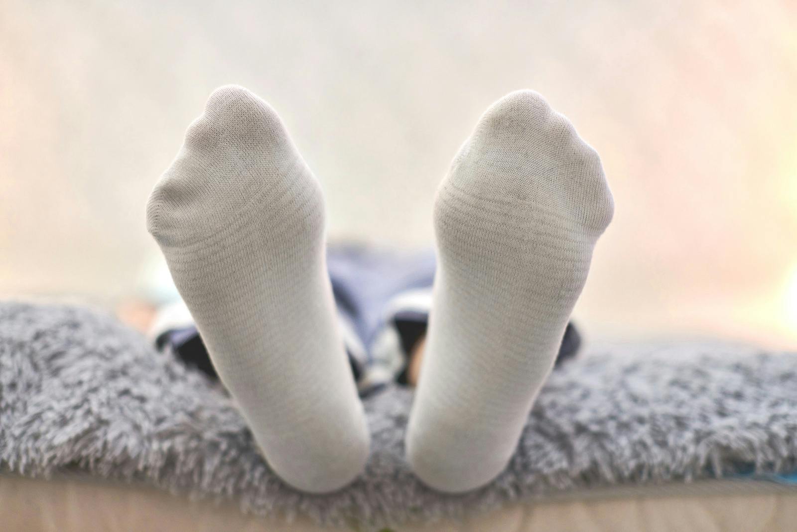 Woman resting on sofa in cozy soft comfortable socks. Female feet in white cotton socks, close up.
