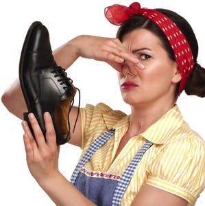 Beautiful vintage housekeeper holding a smelly shoes with facial expression on white
