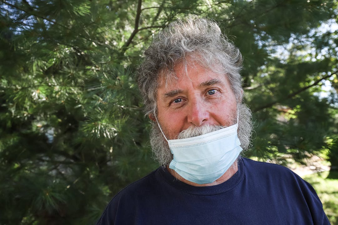 Smiling man wearing medical face mask incorrectly under his nose outdoors
