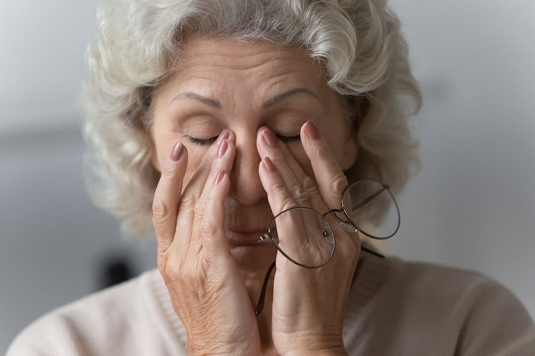 Tired mature woman rubbing nose bridge after taking off eyewear.
