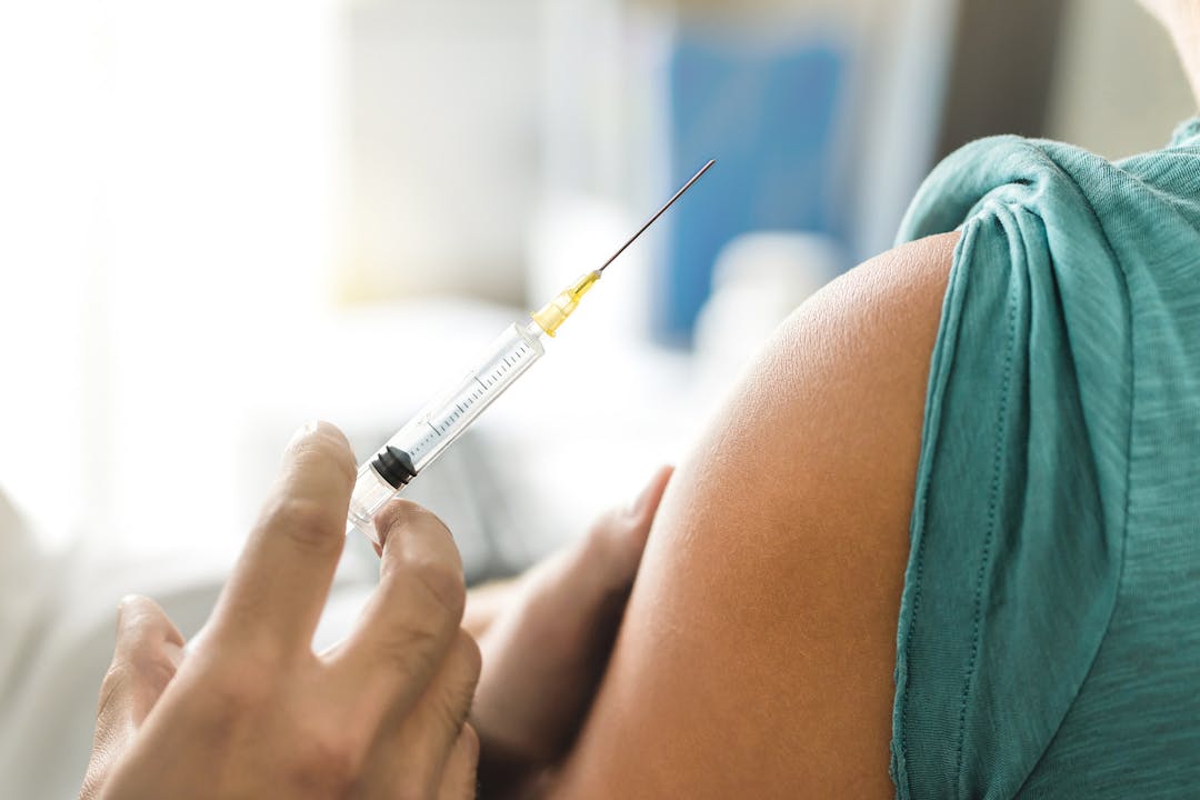 Vaccine or flu shot in injection needle. Doctor working with patient&#8217;s arm. Physician or nurse giving vaccination and immunity to virus, influenza or HPV with syringe. Appointment with medical expert.
