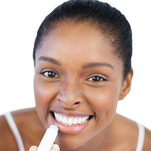 Woman putting lip balm on her lips on white background
