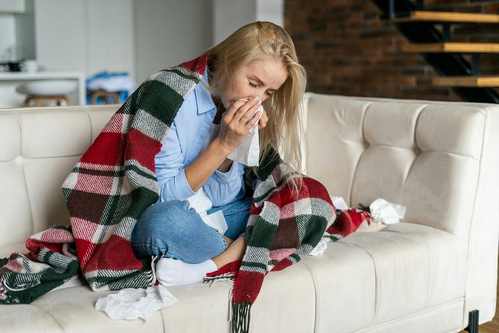 woman sitting on couch surrounded by tissues because of influenza