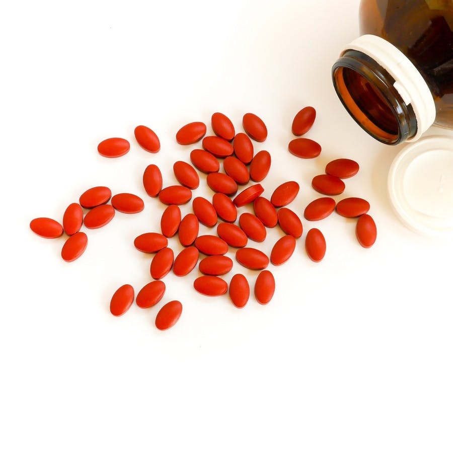 Red iron supplement pills spilling from a pill bottle