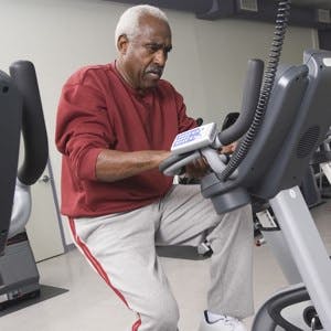 Full length of senior man exercising on stationary bike in health club

