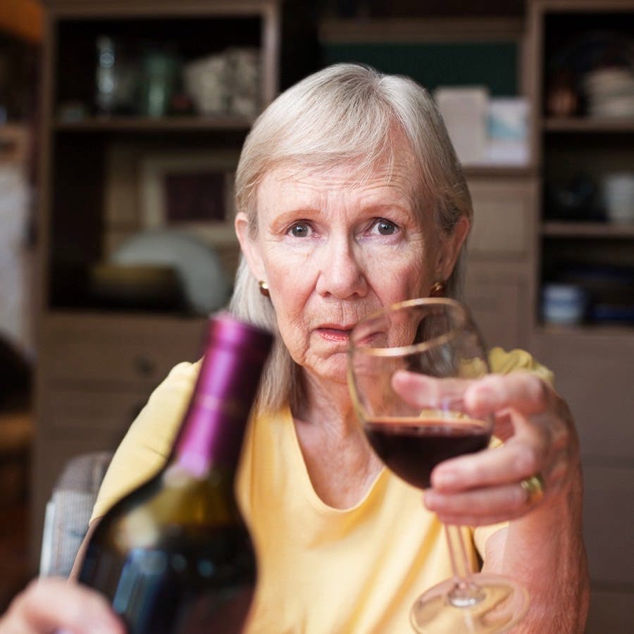Older adult female offering a bottle of wine and glass sitting alone
