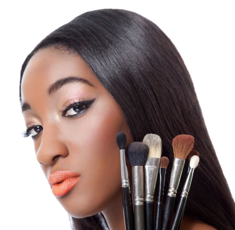 Black woman with straight hair holding makeup brushes isolated on white
