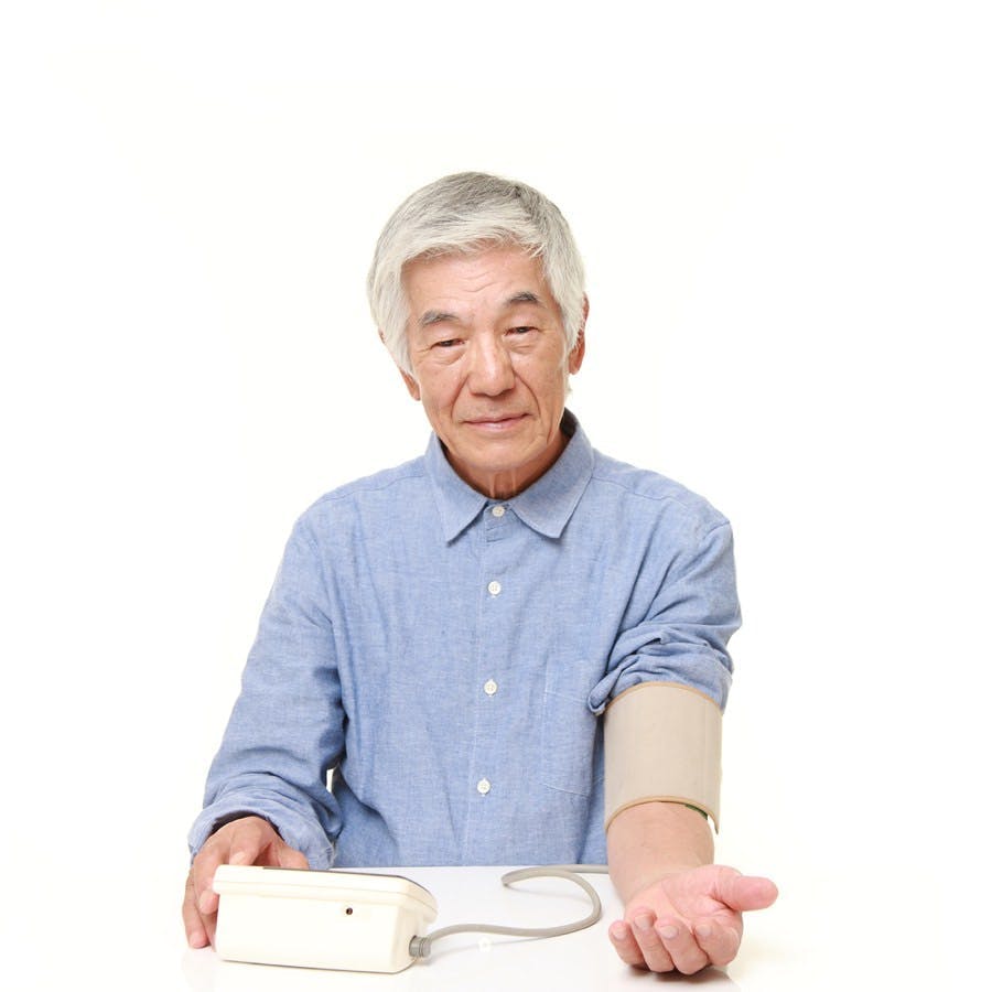 Portrait of senior Japanese man checking his blood pressure on white background
