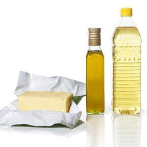 Butter in paper and two bottles of different types of oil on white background

