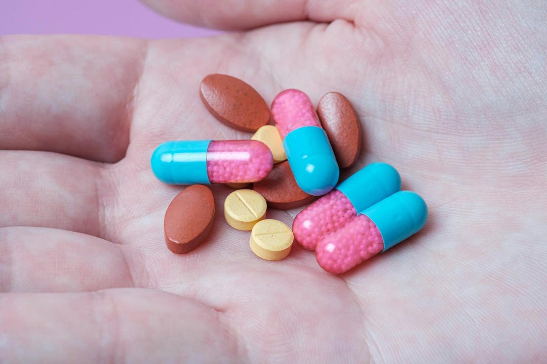 Capsule and pills medicines in hand with pink background
