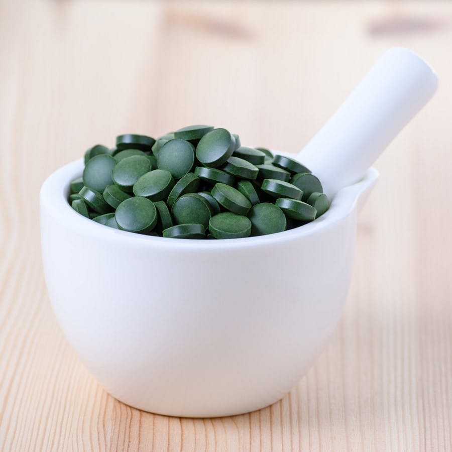 Green spirulina chlorella seaweed pills in a white bowl on the wooden background
