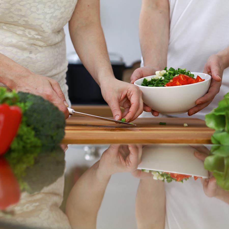 Close-up of  human hands  cooking in a kitchen. Friends having fun while preparing fresh salad. Vegetarian, healthy meal and friendship concept.
