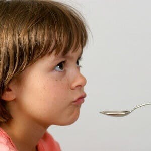 A recalcitrant child stares at a spoon of liquid medicine
