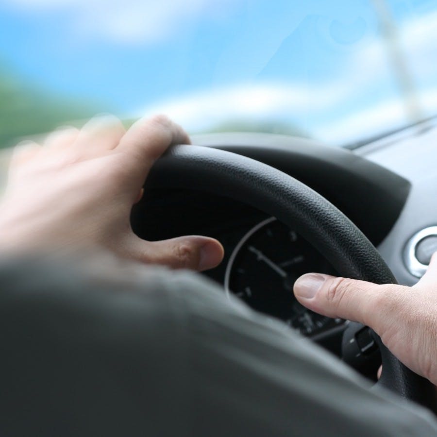 Over shoulder view of a man driving a car with his hands on the steering wheel turning quick. (sunny weather)

