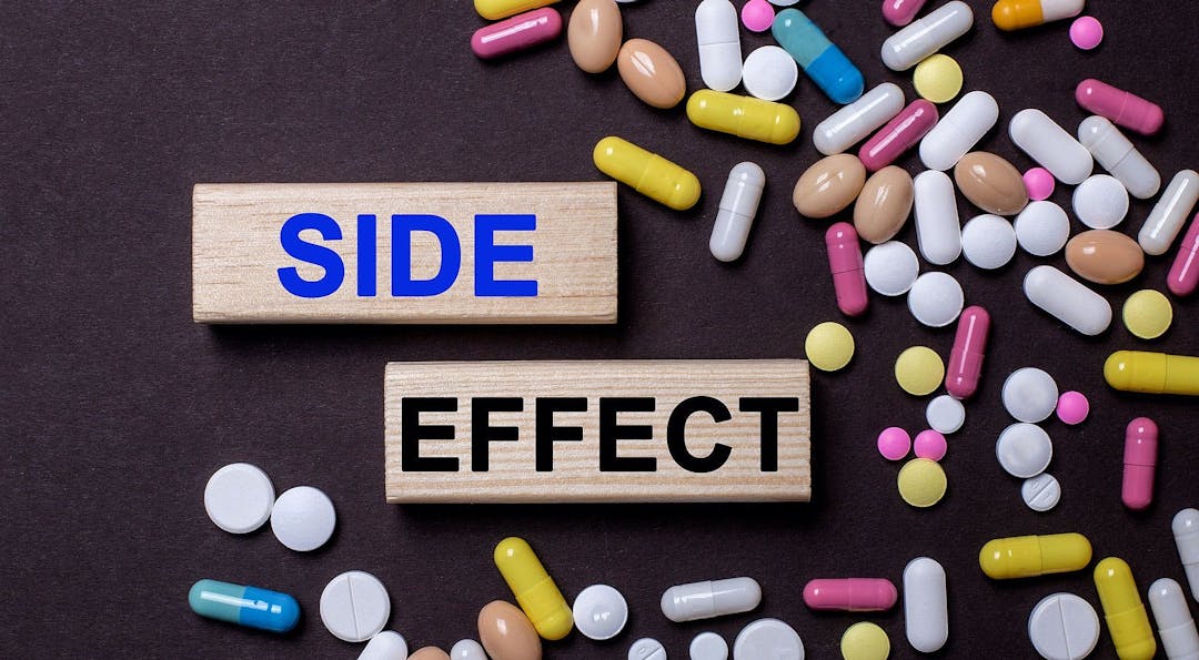 Side effect &#8211; words on wooden printed blocks between multi-colored tablets on a dark background
