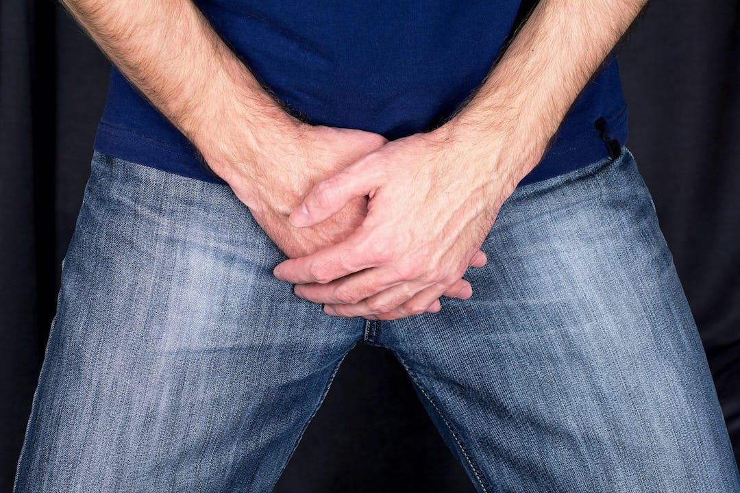 Sexual disorders Erectile dysfunction concept. Close up of a man with hands holding his crotch dark background.

